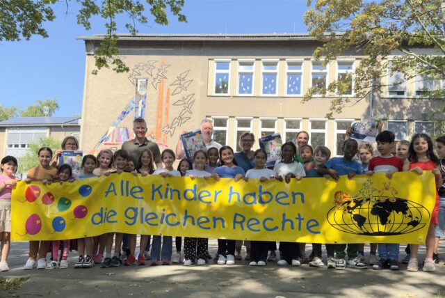 Schüler der Cottenburgschule stehen mit einem breiten Banner. Auf dem steht: Alle Kinder haben die gleichen Rechte.