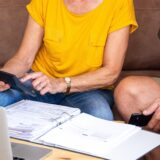 Ein Mann und eine Frau sitzen auf einem Sofa, während vor ihnen auf dem Tisch ein Ordner mit Rentenunterlagen liegt.