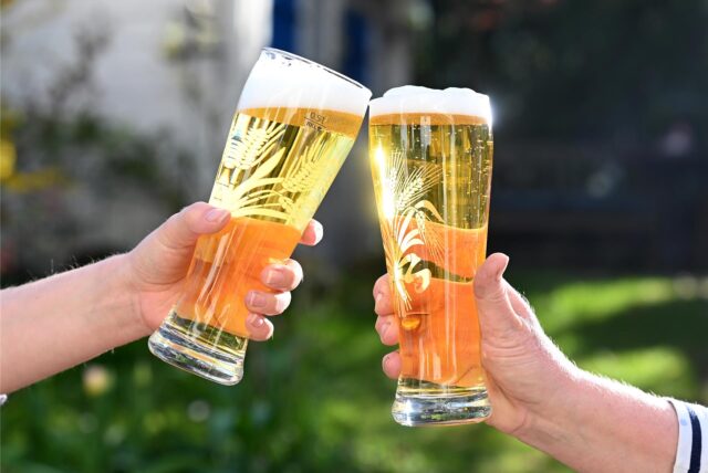 Mit Bier gefüllte Gläser, mit denen zwei Personen anstoßen.