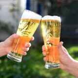 Mit Bier gefüllte Gläser, mit denen zwei Personen anstoßen.