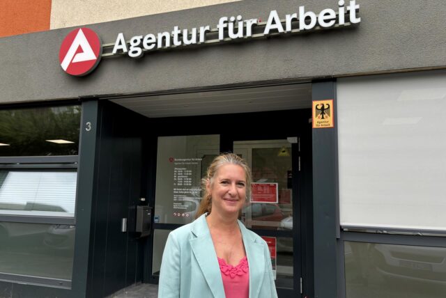 Sandra Haarmann steht vor dem Eingang der Arbeitsagentur in Herten und lächelt in die Kamera.