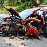 Hagen: Das Auto ist erheblich beschädigt. Polizeibeamte und Feuerwehrkräfte stehen neben dem zerstörten Auto.