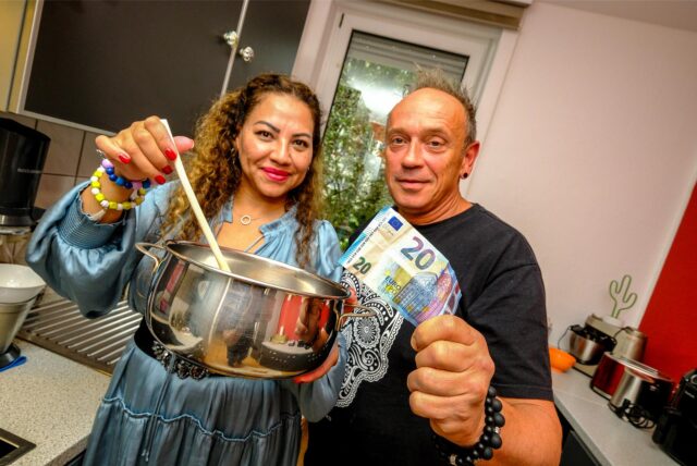 Fabiola Ruschen und Thomas Ernst stehen in ihrer Küche und halten dabei einen Kochtopf und einen 20-Euro-Schein in der Hand.