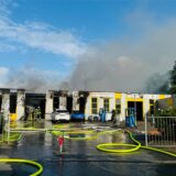 Eine Halle steht in Flammen, eine schwarze Rauchwolke ist zu erkennen.