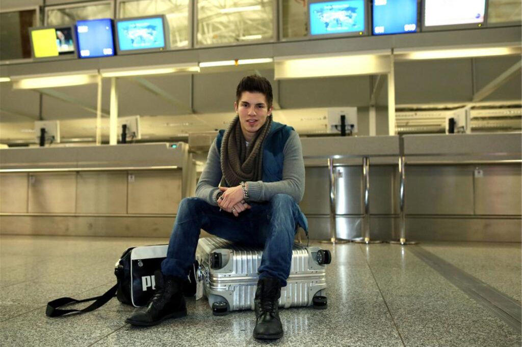 Der Sänger Joey Heindle sitzt vor einem Flughafen-Terminal auf einem Koffer. Der Sänger Joey Heindle sitzt vor einem Flughafen-Terminal auf einem Koffer.