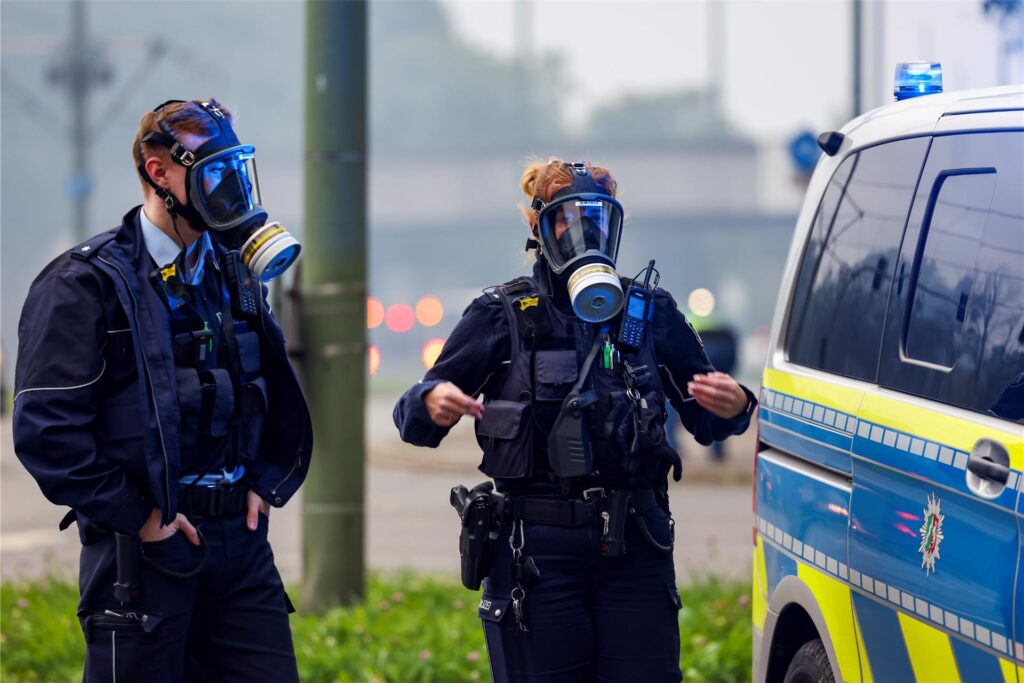 Zwei Polizisten stehen mit Gasmasken im Rauch bei einem Brand in einem Chemiewerk. Zwei Polizisten stehen mit Gasmasken im Rauch bei einem Brand in einem Chemiewerk.