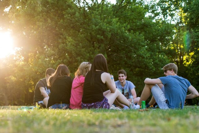 Eine Gruppe Jugendlicher sitzt an einem Sommerabend in einem Park auf der Wiese. (Symbolbild)