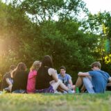 Eine Gruppe Jugendlicher sitzt an einem Sommerabend in einem Park auf der Wiese. (Symbolbild)