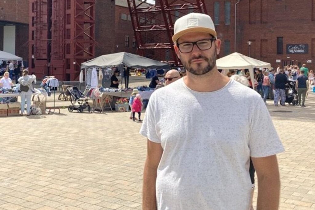 Patrick Barciaga steht auf dem Gelände der Hertener Zeche Schlägel und Eisen. Hinter ihm sind Verlaufsstände zu sehen, an denen einige Menschen vorbeischlendern. Patrick Barciaga steht auf dem Gelände der Hertener Zeche Schlägel und Eisen. Hinter ihm sind Verlaufsstände zu sehen, an denen einige Menschen vorbeischlendern.