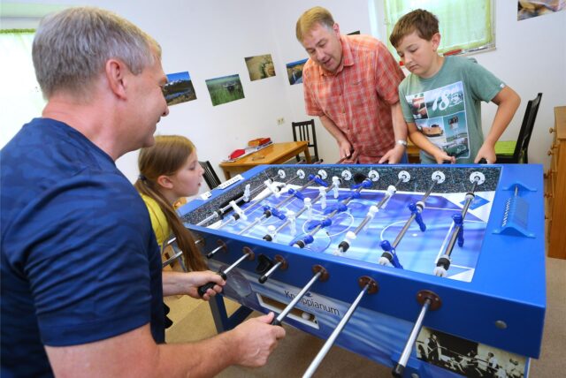 Zwei Männer und zwei Kinder spielen an einem Tischkicker.