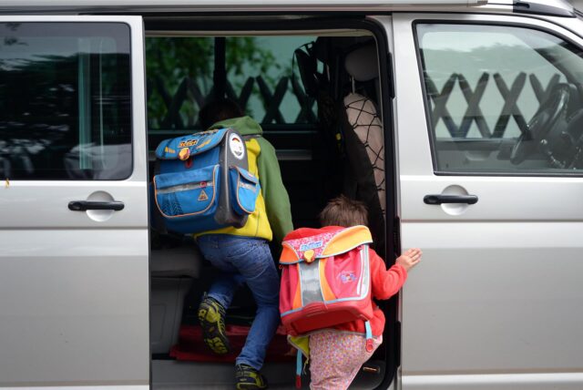 Schulkinder steigen in ein Auto.