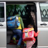 Schulkinder steigen in ein Auto.