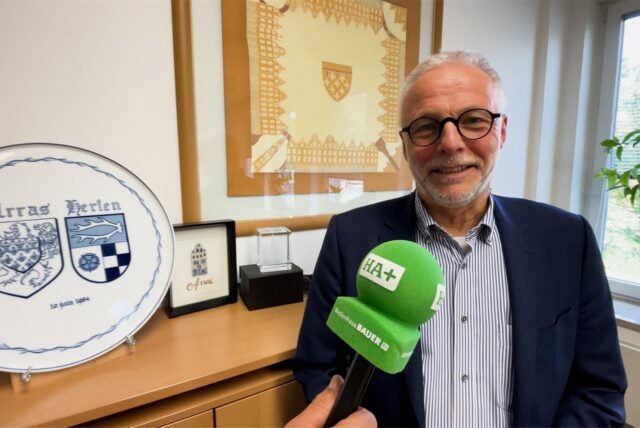 Bürgermeister Matthias Müller lächelt in die Kamera, davor ein Mikrofon der Hertener Allgemeinen.
