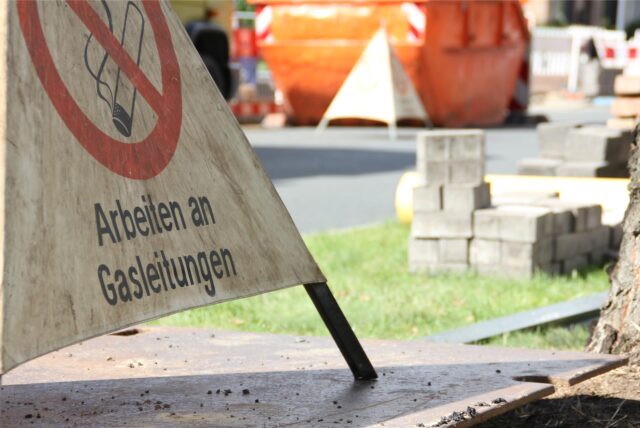 Eine Baustelle mit einem Schild im Vordergrund, auf dem „Arbeiten an Gasleitungen“ steht.