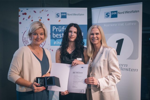 Zwei Frauen der IHK verleihen eine Urkunde an eine Auszubildende.