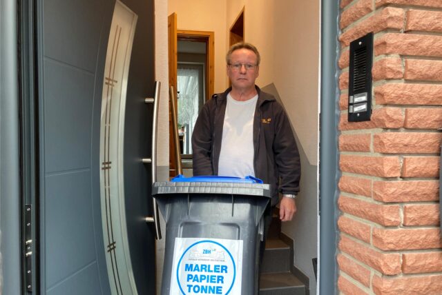 Ein Mann, der mit einer Mülltonne vor dem Haus steht.