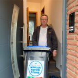 Ein Mann, der mit einer Mülltonne vor dem Haus steht.