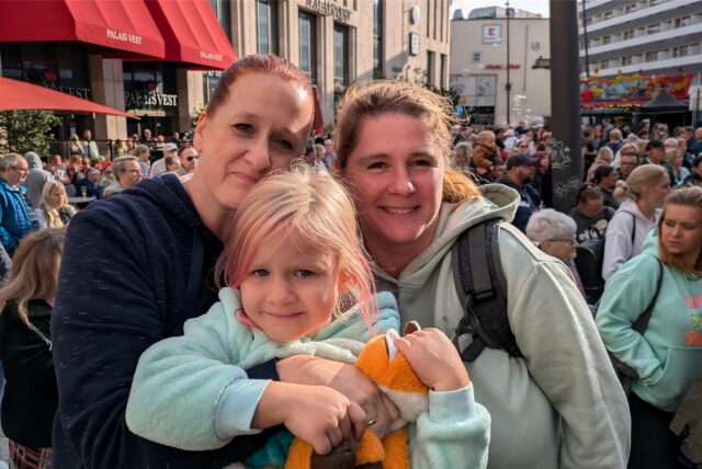 Zwei Frauen und ein Mädchen schauen in die Kamera. Dahinter sind das Palais Vest und der mit vielen Menschen gefüllte Löhrhof in Recklinghausen zu sehen.