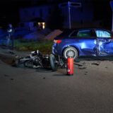 Motorradt liegt auf der Straße vor einem blauen Auto mit beschädigter Beifahrerseite.
