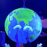 In einer Manege stehen mehrere Mädchen, über ihnen strahlt eine Weltkugel. Die Manege ist in blaues Licht getaucht.
