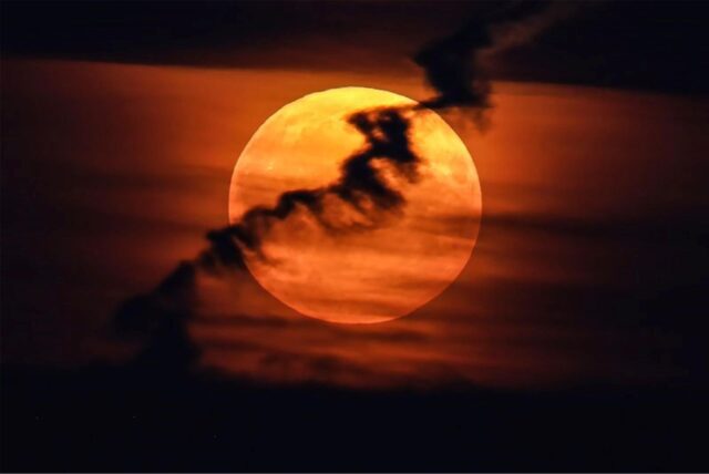 Ein großer Vollmond erscheint hinter Wolken am roten Abendhimmel. Da er näher an der Erde ist als sonst und damit größer erscheint, wird er als Supermond bezeichnet.