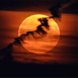 Ein großer Vollmond erscheint hinter Wolken am roten Abendhimmel. Da er näher an der Erde ist als sonst und damit größer erscheint, wird er als Supermond bezeichnet.