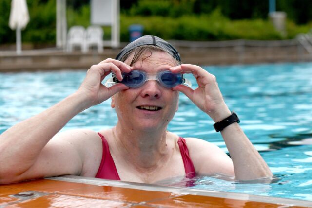Eine Frau ist im Freibad des Hertener Copa Backum am Beckenrand und richtet ihrer Schwimmbrille, um die nächste Bahn ziehen zu können.