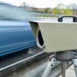 Ein blaues Auto fährt an einem Blitzer vorbei.