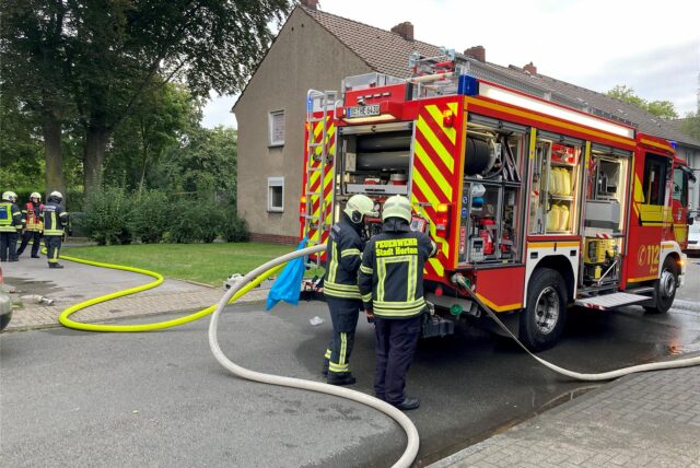 Ein Löschfahrzeug der Feuerwehr, an dem Schläuche angeschlossen sind, steht auf einer Straße.