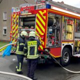 Ein Löschfahrzeug der Feuerwehr, an dem Schläuche angeschlossen sind, steht auf einer Straße.