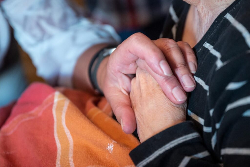 Eine große, männliche Hand hält die Hand einer alten Dame. Eine große, männliche Hand hält die Hand einer alten Dame.