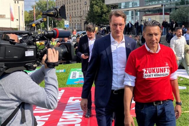 Nordrhein-Westfalens Ministerpräsident Hendrik Wüst (CDU, M) und Tekin Nasikkol, Konzernbetriebsratsvorsitzender von Thyssenkrupp, kommen zu einer Demonstration vor dem „Nationalen Stahlgipfel“ des Wirtschaftsministeriums von Nordrhein-Westfalen vor der Mercatorhalle.