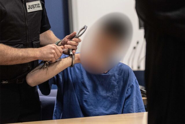 Ein Justizbeamter nimmt dem 24-jährigen Angeklagten, der eine 17-Jährige mit Benzin übergossen und angezündet haben soll, zu Prozessbeginn im Landgericht die Handschellen ab.