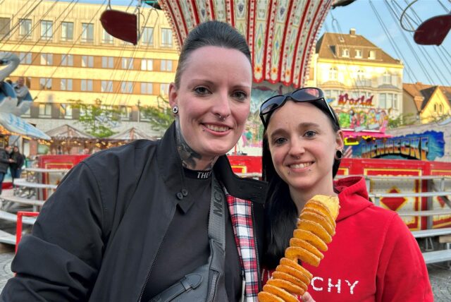 Zwei Besucher der Castroper Herbstkirmes stehen vor einem Karussell auf dem Marktplatz.