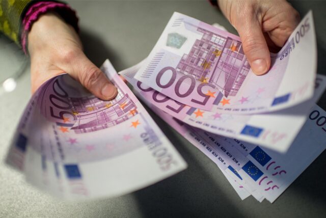 Zwei Hände halten 500 Euro Scheine. Die Person zählt sie durch.
