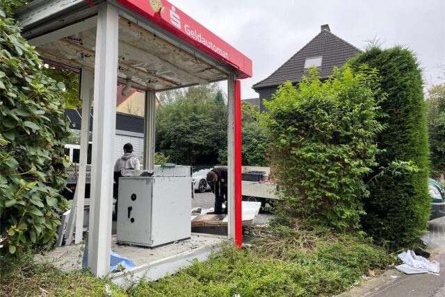 Am Tag nach der Geldautomaten-Sprengung in Dortmund-Oespel sicherten Handwerker den zerstörten Container. Ein Teil des Geldautomaten blieb heil.