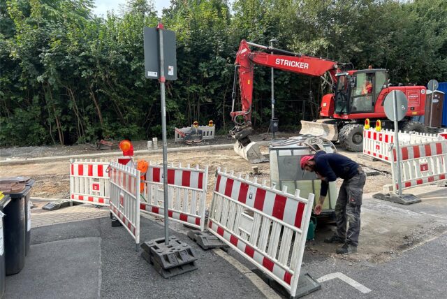 Zwei Bauarbeiter bereiten die Thomasstraße mit einem Bagger für den Asphalteinbau vor.