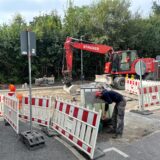 Zwei Bauarbeiter bereiten die Thomasstraße mit einem Bagger für den Asphalteinbau vor.