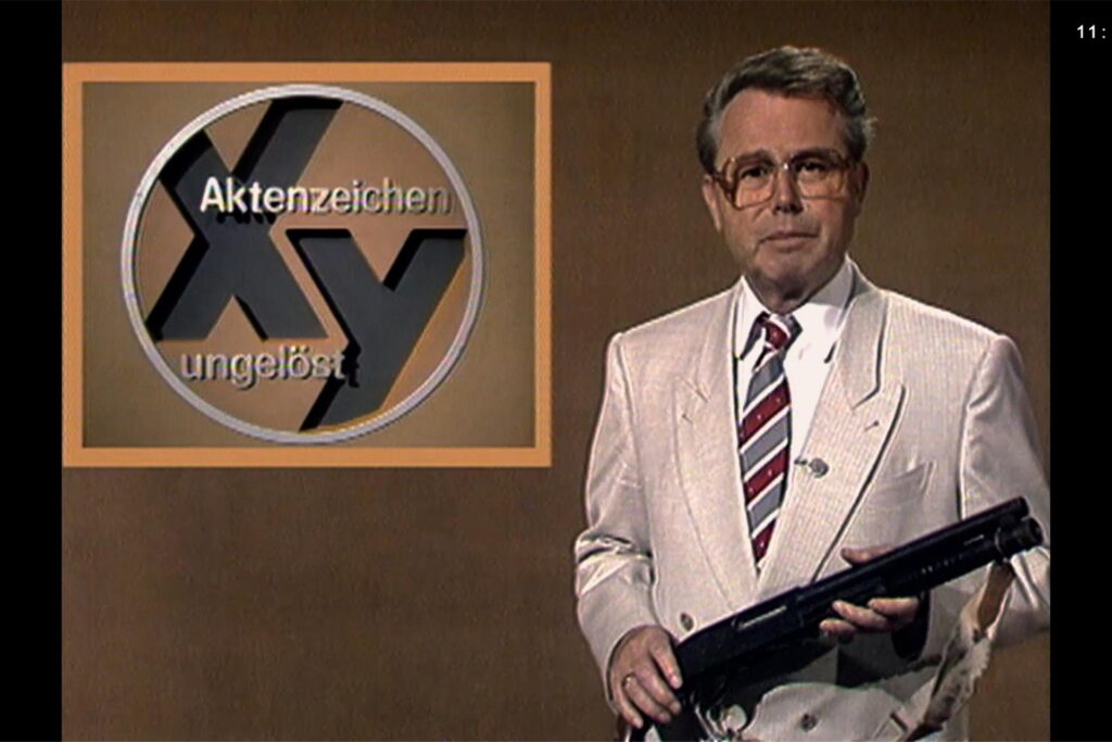 Moderator Eduard Zimmermann steht vor einem braunen Hintergrund mit dem Sendungslogo Moderator Eduard Zimmermann steht vor einem braunen Hintergrund mit dem Sendungslogo