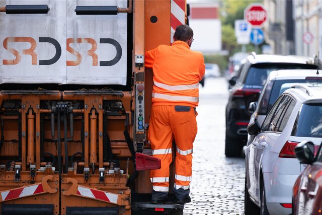 Ein Müllwerker fährt auf einem Müllfahrzeug mit.