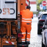 Ein Müllwerker fährt auf einem Müllfahrzeug mit.