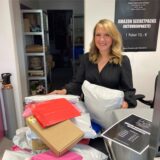 Die Hertenerin Julia Azam steht in ihrem Kiosk in Herten an einem Tisch, auf dem einige der Amazon-Secretpacks liegen.