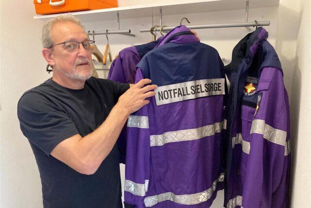 Der Hertener Notfallseelsorger greift an einer Garderobe zu einem Bügel, auf dem seine Einsatzjacke hängt.