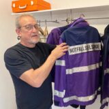Der Hertener Notfallseelsorger greift an einer Garderobe zu einem Bügel, auf dem seine Einsatzjacke hängt.