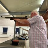 Alfred Simon steht auf der Schießbahn der Bürgerschützengilde in Westerholt. Er kontrolliert das Visier an seinem Luftgewehr. Der Lauf zeigt nach Links auf die Zielscheiben außerhalb des Bildes.
