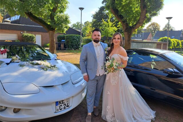 Ein Hochzeitspaar in Herten steht neben zwei feierlich geschmückten Autos.