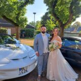 Ein Hochzeitspaar in Herten steht neben zwei feierlich geschmückten Autos.
