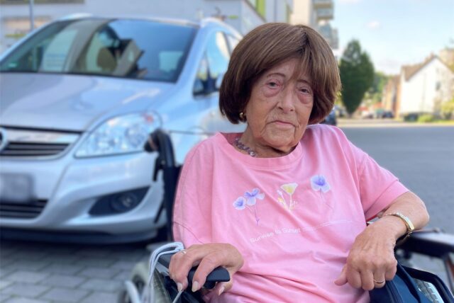 Christel Schürmann sitzt in einem Rollstuhl vor dem Theodor-Fliedner-Haus in Herten-Westerholt. Hinter ihr parkt ein silberfarbener Opel.