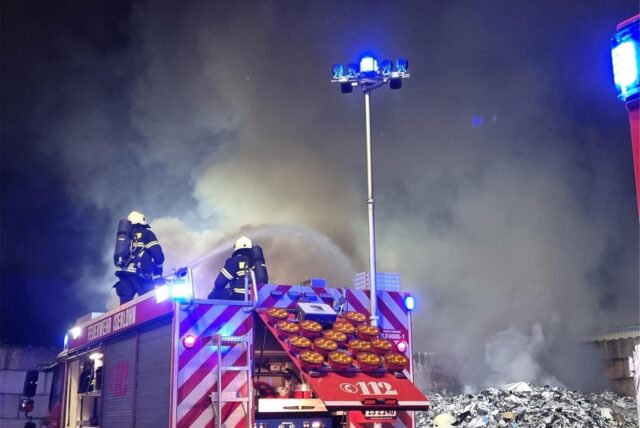Ein Feuerwehrfahrzeug mit Einsatzkräften, die gerade den Brand im Entsorgungsbetrieb löschen.