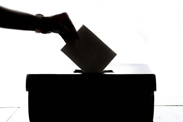 Eine Hand wirft einen Zettel in eine Wahlurne.